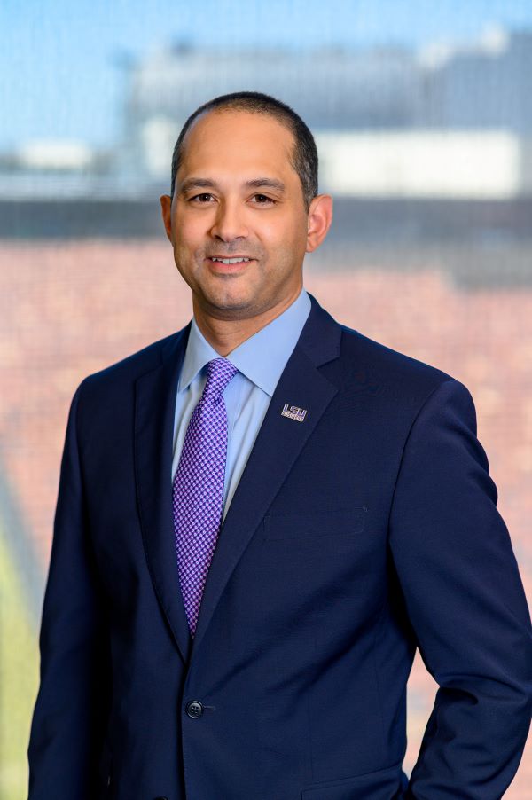 Jared Llorens standing in front of a window. He is wearing a blue suit and a tie. 