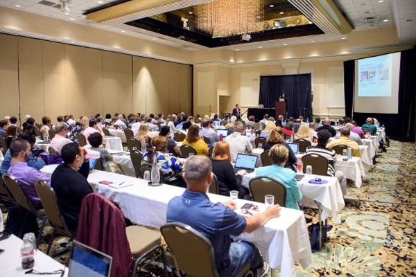 Ball room filled with seated conference attendees. 