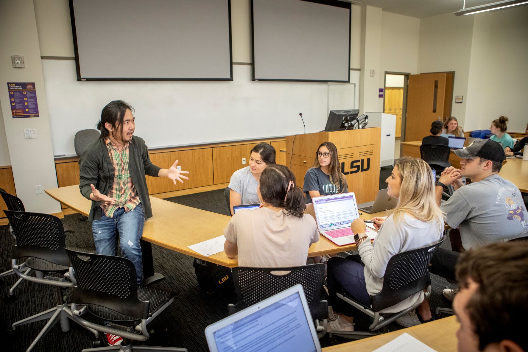 Professor sits on desk and talks to students. 