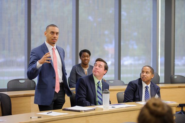 Male student stands to speak while others look on. 