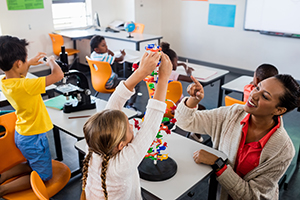 Photo of a teacher helping young children with building blocks.