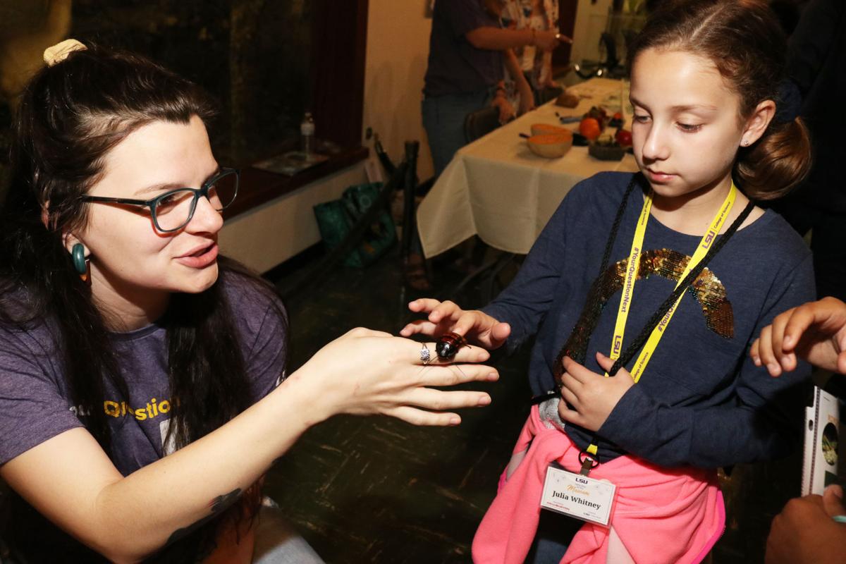 Girls' Day at the Museum participants pets a hissing cockroach as a student researcher tells her about the speices.